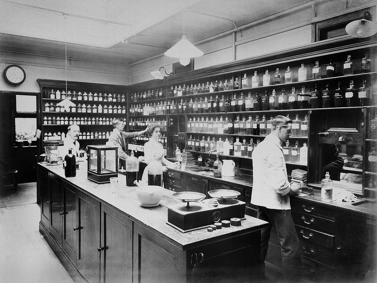 A London hospital dispensary in about 1900: shelves of labelled bottles, scales and a long counter